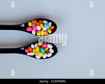 Multi colored sweet fennel sugar candy in black spoons against white background with copy space, isolated Stock Photo