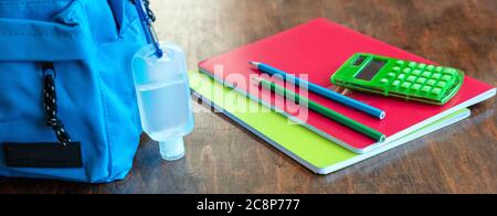 School, coronavirus days. Hand sanitizer gel and school bag backpack on wooden desk background, close up view, banner Stock Photo