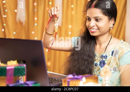 Indian Woman in tradition dress on video call or chat at Raksha Bandhan festival telling her brother to tie rakhi - Concept of distance relations Stock Photo