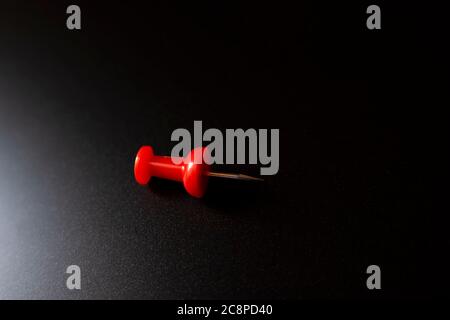 A closeup shot of a single plastic handled red pushpin on a black surface Stock Photo