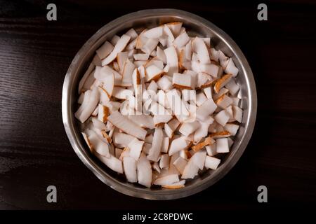 a top view of fresh coconut flakes pieces in bowl on dark wooden table Stock Photo