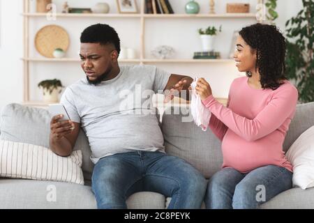 Happy pregnant woman showing busy husband baby clothes Stock Photo