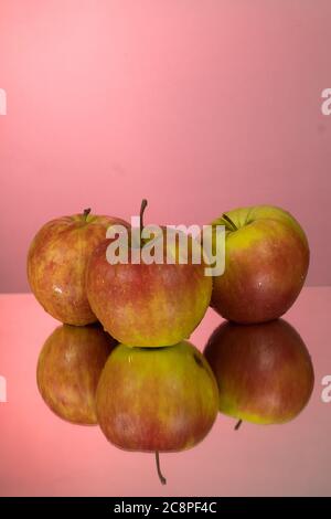 Three red apples on mirroring table on mirror red background with reflection isolated close up Stock Photo