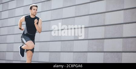 Fast running on training in city. Athletic man in sportswear with fitness tracker runs and jumps Stock Photo