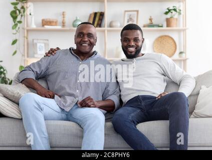 Adult black son and his senior father posing on couch at home Stock Photo