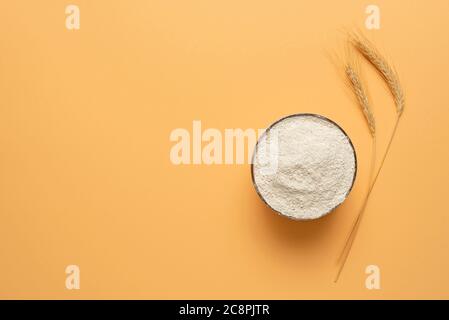 Bowl of wholemeal flour isolated on a beige background. Top view with a bowl of wholemeal flour and two ears of wheat Stock Photo