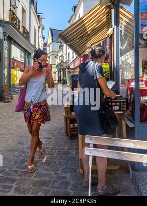 Young woman putting on face-mask before entering shop - Loches, Indre-et-Loire, France. Stock Photo
