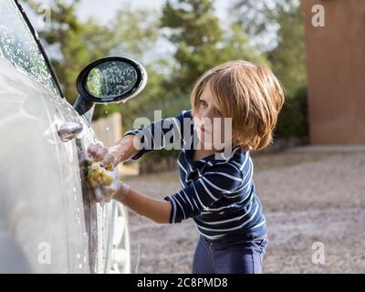 Four year old boy washing a car with cleaner and a cloth Stock Photo