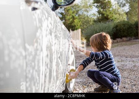 Four year old boy washing a car with cleaner and a cloth Stock Photo