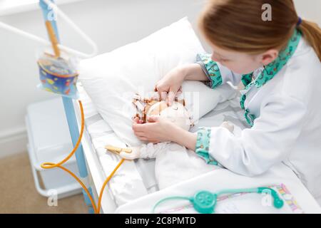 Young girl dressed as doctor putting plaster on doll's head in make-believe hospital bed Stock Photo