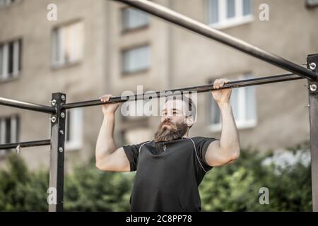 Young man doing pull-up on horizontal bar. Mans fitness at the stadium Stock Photo