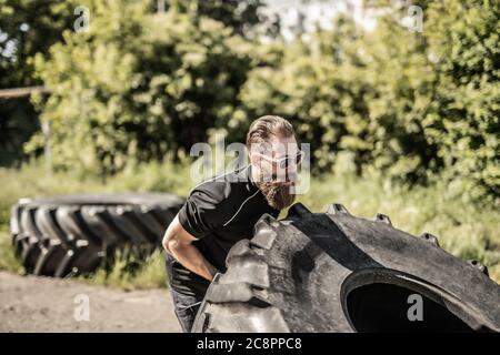 Full length side view of young male athlete flipping large tire outside gym Stock Photo