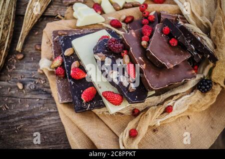 Chocolate mix with nuts and dried fruits on rustic wooden background. Chocolate blocks stack with different kind of chocolate. Chocolate bar pieces Stock Photo