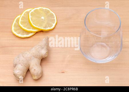three round slices of lemon, a piece of light-brown ginger and an empty water glass on a wooden surface, ingredients for healthy vitamin drink on a wood table, preparation of energy seasonal lemonade Stock Photo