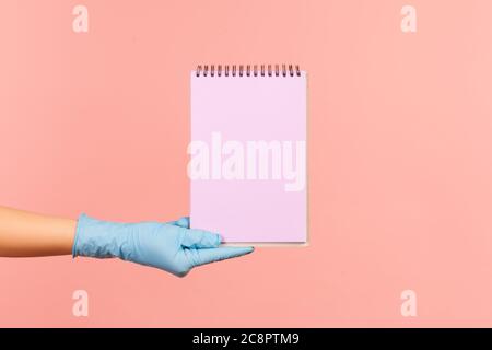 Profile side view closeup of human hand in blue surgical gloves holding purple notepad in hand and holding empty paper. indoor, studio shot, isolated Stock Photo