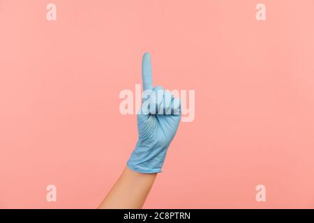 Profile side view closeup of human hand in blue surgical gloves showing number one with finger or showing up side. indoor, studio shot, isolated on pi Stock Photo