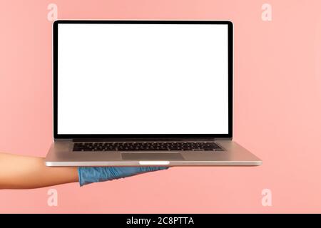 Profile side view closeup of human hand in blue surgical gloves holding computer laptop and showing empty copy space on monitor screen. indoor, studio Stock Photo
