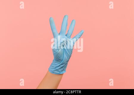 Profile side view closeup of human hand in blue surgical gloves showing number four 4 with hand. indoor, studio shot, isolated on pink background. Stock Photo
