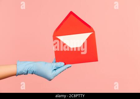 Profile side view closeup of human hand in blue surgical gloves holding red opened letter envelope. indoor, studio shot, isolated on pink background. Stock Photo