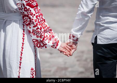 Newlyweds hold hands, dressed in red embroidery Stock Photo