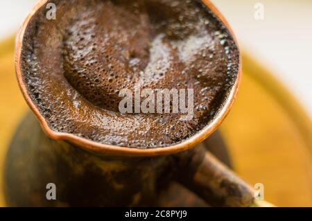 Natural coffee with thick foam, brewed in a copper cezve in the classical way, on a wooden background, macro photo. Stock Photo