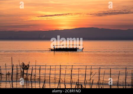 Sunset pier Albufera Valencia tourist ride boat reflections orange sky in the lake Natural Park Spain. traditional fishing nets in the water Stock Photo