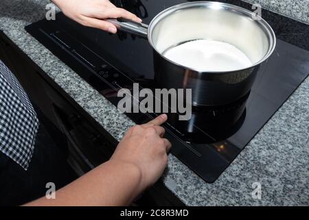 Female hand turns on electric hob closeup. Cooking Milk to make apple cake Stock Photo