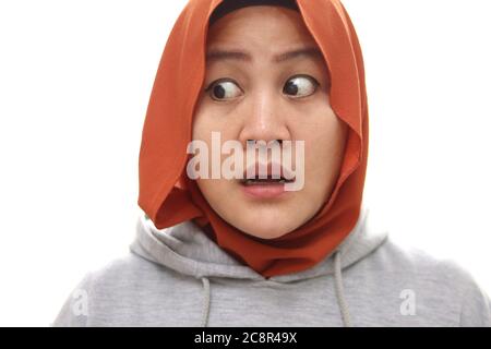 Asian muslim woman wearing hijab stuned shocked expression looking to the side with big eyes and open mouth. Isolated on white.