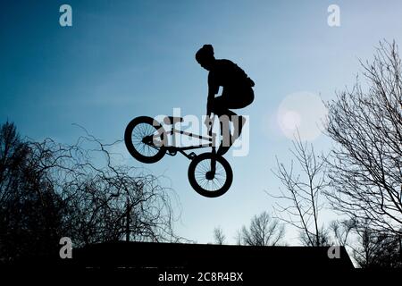 View from below strong athlete jumping in air. Guy performs tricks on a bike. Concept of adrenaline. Stock Photo