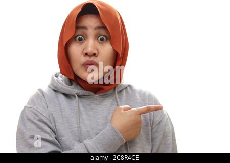 Portrait of astonished Asian muslim woman iwearing hijab feeling amazed and pointing to the side on copyspace isolated over white Stock Photo