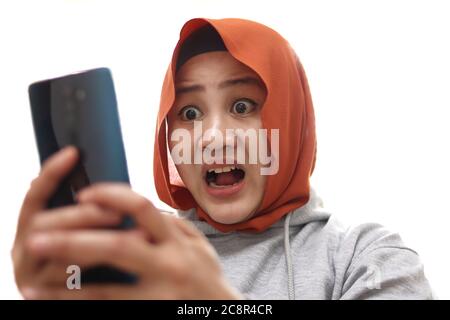 Shocked worried Asian muslim woman worried when reading bad news text message on her smart phone isolaed on white Stock Photo