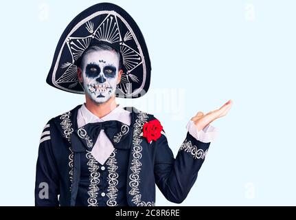 Young man wearing day of the dead costume over background smiling cheerful presenting and pointing with palm of hand looking at the camera. Stock Photo