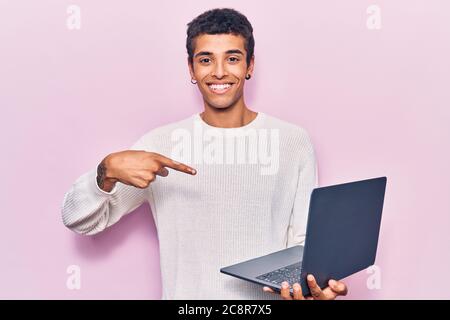 Young african amercian man holding laptop smiling happy pointing with hand and finger Stock Photo