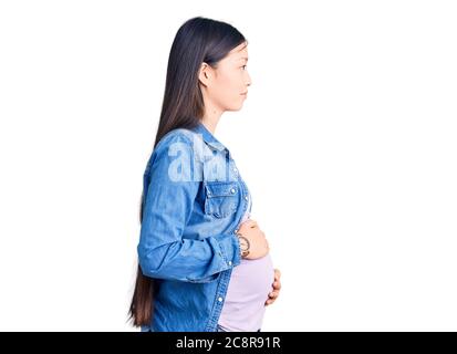 Young beautiful chinese woman pregnant expecting baby looking to side, relax profile pose with natural face and confident smile. Stock Photo