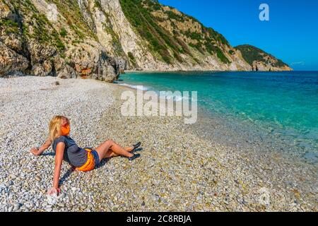 Lifestyle woman with orange surgical mask resting sunbathing in Sansone beach during Covid-19 looking the and blue sea. Tourism in Elba island and Stock Photo