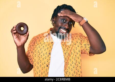 Young african american man with braids holding donut stressed and frustrated with hand on head, surprised and angry face Stock Photo