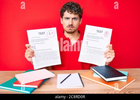 Young caucasian man with curly hair showing a passed exam sitting on the table skeptic and nervous, frowning upset because of problem. negative person Stock Photo