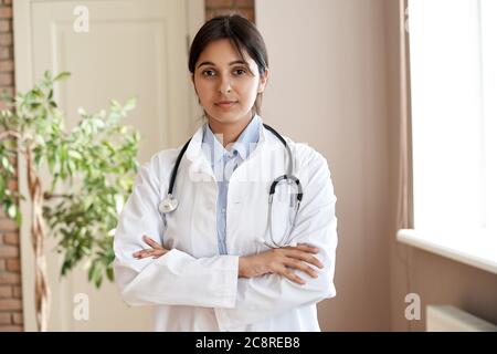 Confident indian female doctor wear white coat look at camera stand arm crossed. Stock Photo