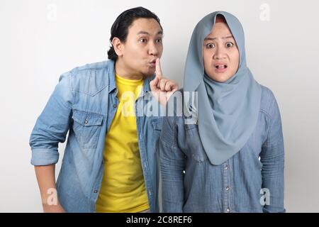 Asian man tells a secret to her woman and ask to keep silence, shocked surprised expression to hear gossip Stock Photo