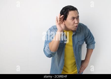 Young asian men wearing blue shirt listen whispers with funny face. Curious. Intently listen in on juicy gossip. Conversation news, privacy violation, Stock Photo