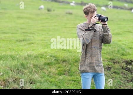 Photographer standing on a grass hill taking picture. Large copy space for text or illustration at side of image. England, UK. Young, stylish, trendy Stock Photo