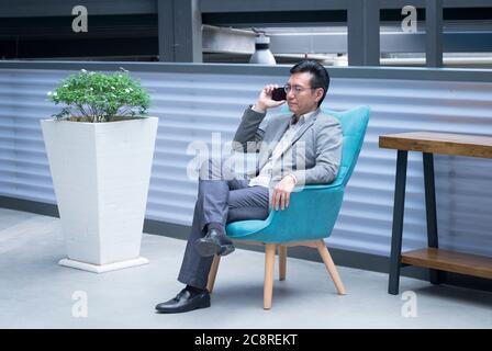 Chinese businessman sitting on a chair and having a phone call via his cellphone Stock Photo