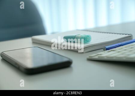 Highlighter pen on top of notepad, with cellphone and keyboard on office table Stock Photo