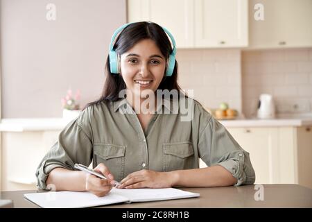 Happy indian girl wear headphones look at camera study at home listen course. Stock Photo