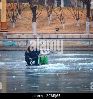 Tianjin, China - Jan 16 2020: Unidentified people ice fishing in the middle of a frosty river Haihe Stock Photo