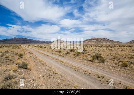 Small cliffs and rock formations of the Utah West Desert. Leading toward a distant mountain is a small dirt track through the sagebrush. Stock Photo