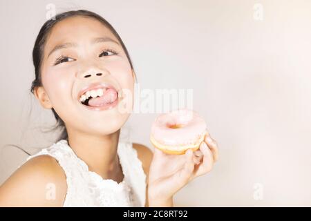A cute Asian girl is enjoying eating donuts. Stock Photo