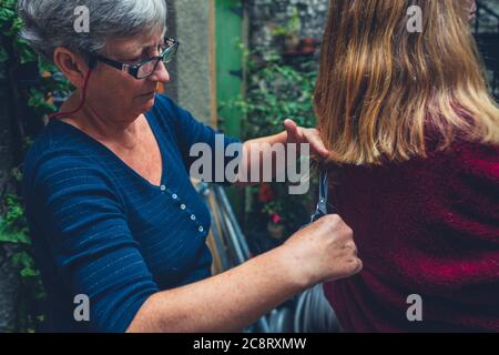 A senior woman is cutting a young womans hair outdoors Stock Photo