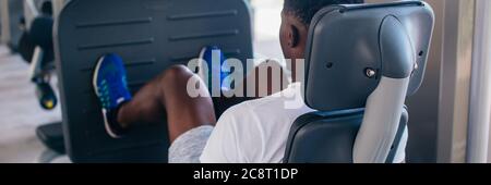 Back view of African American man doing exercise on leg press during fitness training in modern gym. Stock Photo