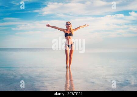 happy girl with her arms outstretched stands in the water. Beautiful reflection of the cloudy sky in the lake. Young woman standing on the shore of Stock Photo